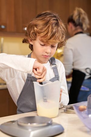 Adorable kid stirring liquid ingredient while baking with mother