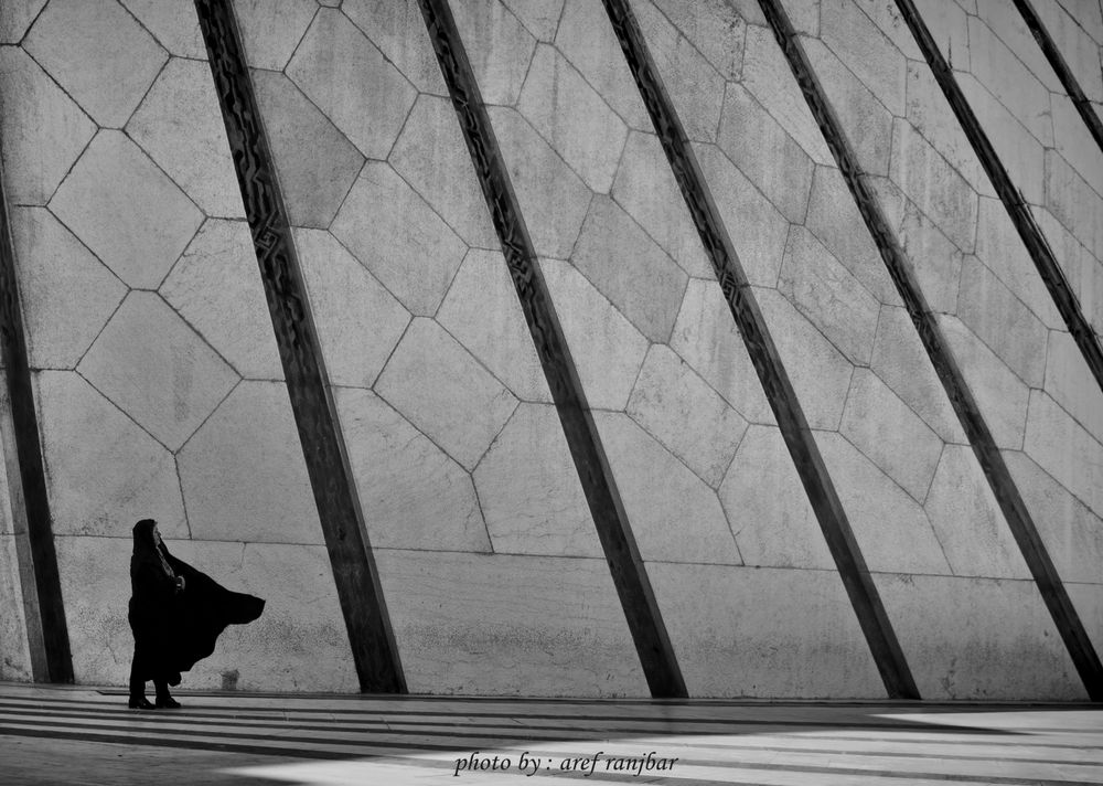 Grayscale photo of woman wearing burqa standing beside a wall in Iran