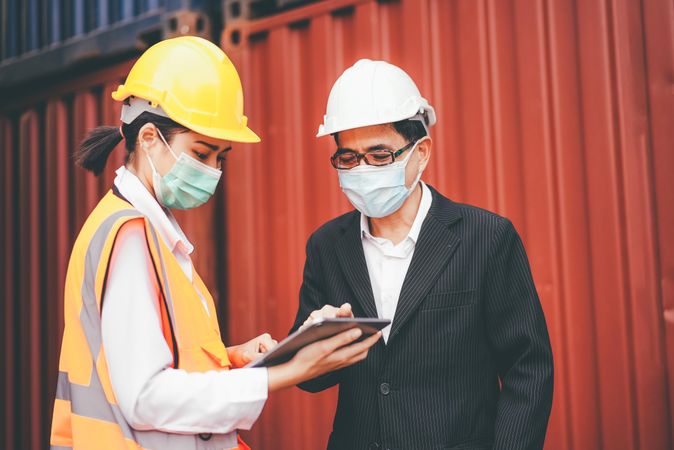 Asian logistic foreman wearing protective mask with female worker with tablet