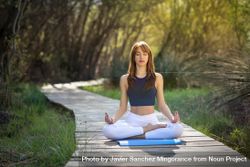 Female wearing sport clothes meditating with eyes closed on yoga mat outside 4d2PE0