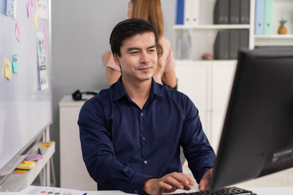 Man sitting at his office desk typing on keyboard and looking at monitor