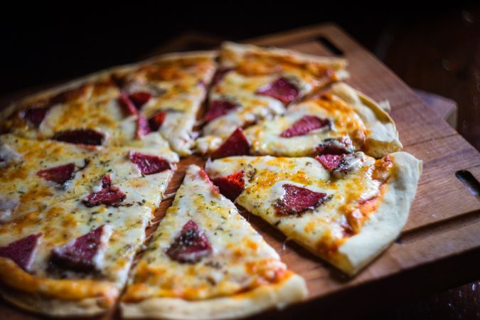 Delicious pizza with slices of meat on wooden board
