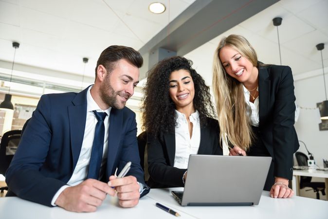 Multi-ethnic co-workers together in office around a laptop