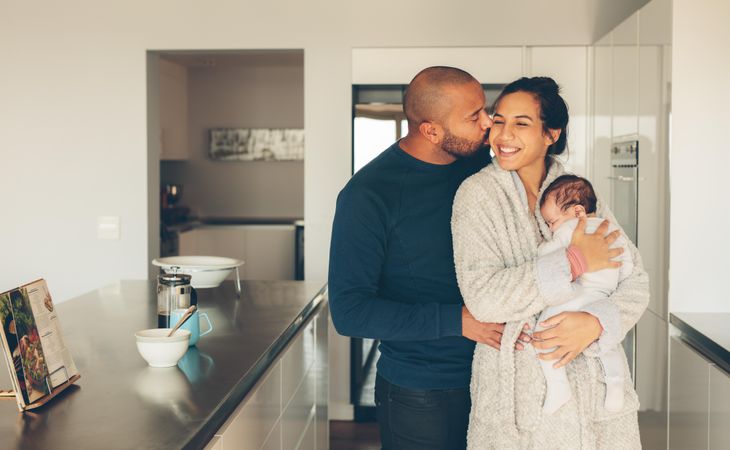 Loving young couple with their newborn baby boy in kitchen