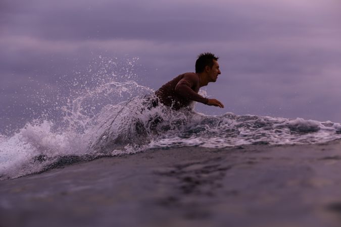 Man on surf board floating on water and cloudy sky