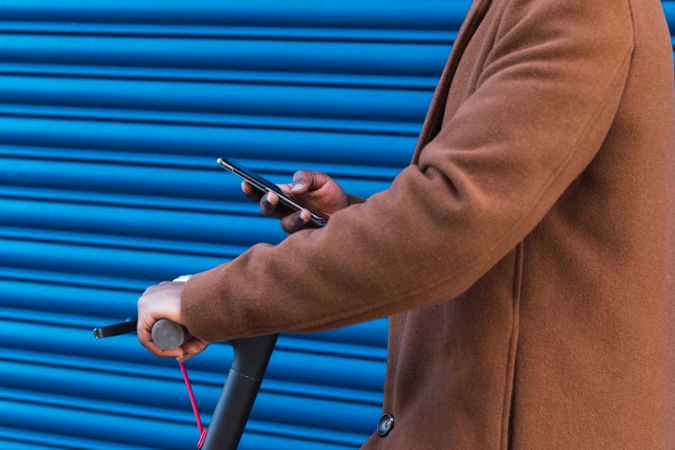Anonymous stylish Black man with electric scooter using smartphone