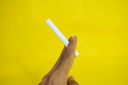 Side view of hand holding cigarette against yellow wall