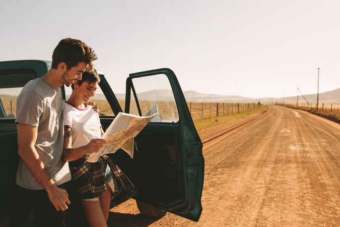 Young couple standing beside classic truck on open road holding map while on road trip