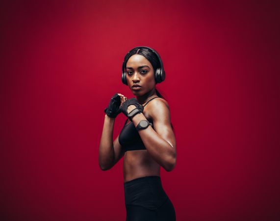 Young woman wearing boxing gloves posing in combat stance looking at camera