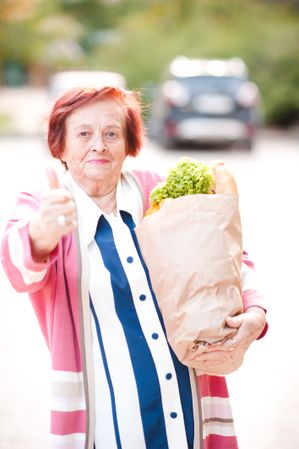Older woman in pink cardigan holding grocery bag standing outdoor