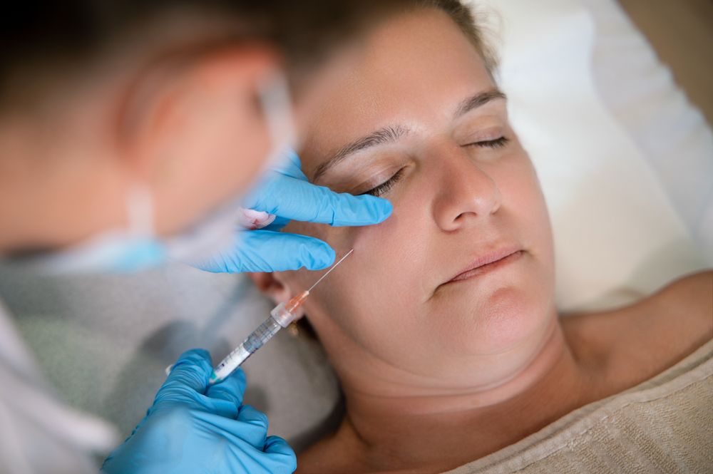 Faceless cosmetologist administering facial rejuvenating injection to client