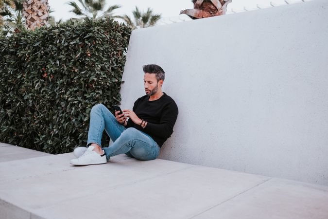 Adult stylish smiling man using a smartphone near grey wall