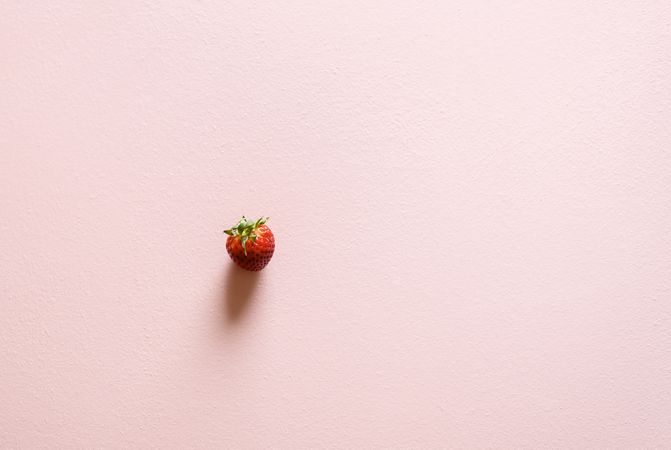 Single organic strawberry on a pink table