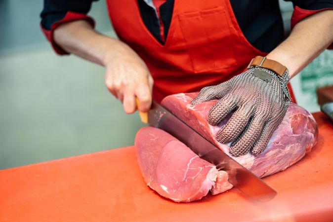 Close up of butcher in apron slicing chunk of raw meat