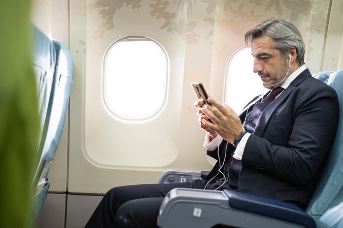 Grey haired man using smartphone in flight