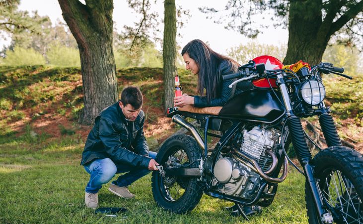 Man fixing his motorcycle while his girlfriend looks at him