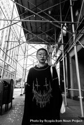 Grayscale photo of woman in long dress standing under scaffolding on sidewalk 0yMMn0