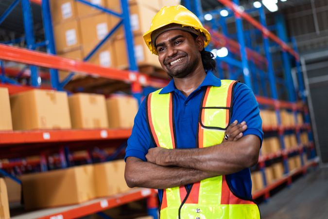 Smiling Indian warehouse worker with arms crossed in safety gear