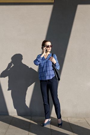 Businesswoman having smartphone conversation near gray wall