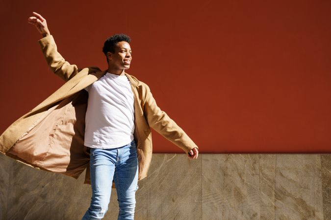 Black male in camel coat with one arm above head