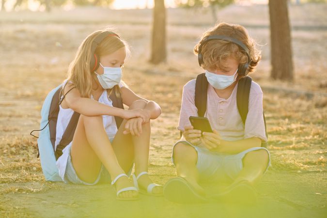Children watching video on smartphone while sitting on ground in