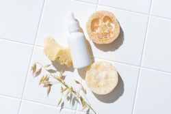 Loofah and bottle of serum on bathroom floor