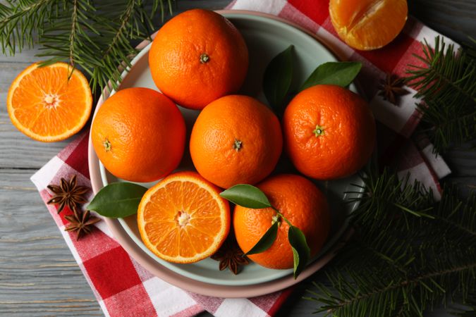 Plates with mandarins, pine branches, napkin and cinnamon on wooden background