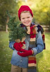 Young Boy Wearing Holiday Clothing Holding Small Christmas Tree Outside