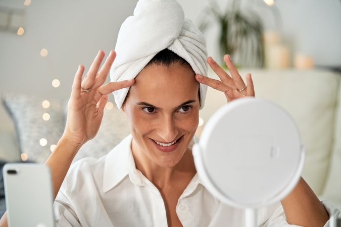 Cheerful woman doing face massage looking at mirror