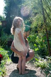 Mother puts arm around  daughter on rock path looking at plants with child looking at camera