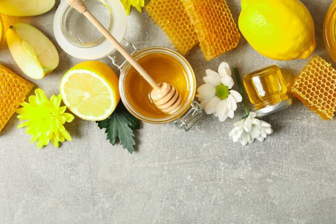 Flat lay with honey, flowers and fruits on grey background, copy space