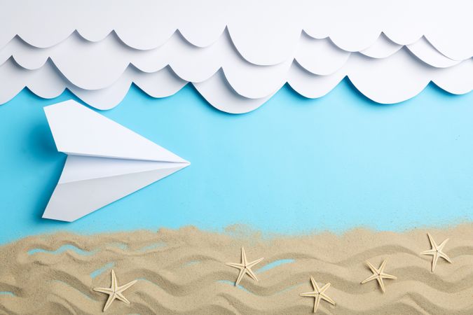 Paper clouds and plane, sand with starfishes on blue background. Vacation
