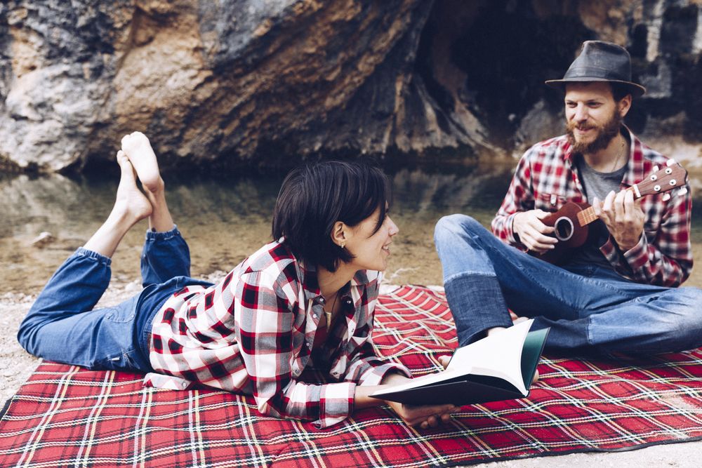Chilling couple with book and guitar on shore