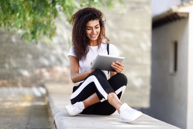 Smiling Arab woman looking down at her digital tablet while sitting outdoors
