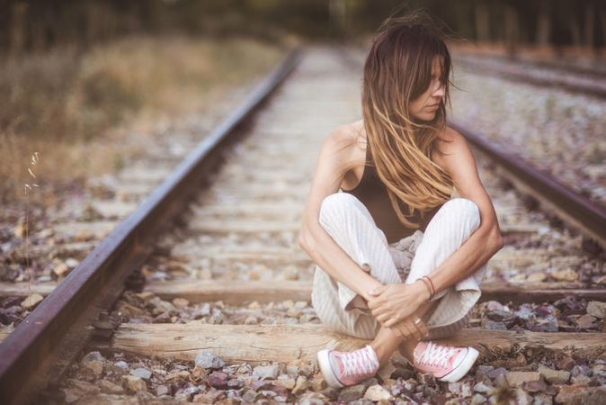 Long haired woman sitting on railways overgrown with dry grass