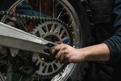 Crop mechanic changing motorbike chain in workshop