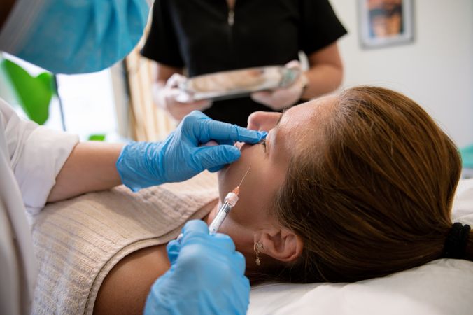 Beauty specialist applying cosmetic product with syringe on face of client in clinic
