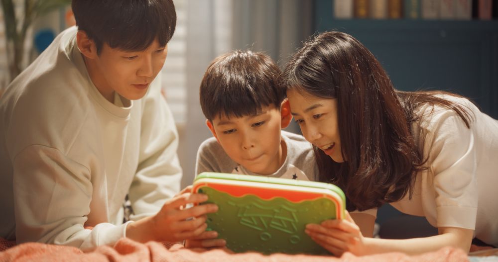 Idyllic Young South Korean Family Spending Leisure Time Together at Home, Watching Cartoons Online and Playing Educational Video Games