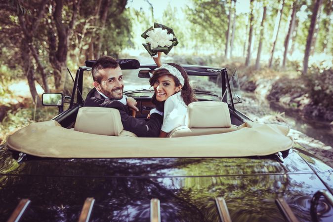 Newlyweds with bouquet  looking back in vintage car