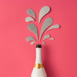 Champagne bottle with silver glittering splashes on pink background
