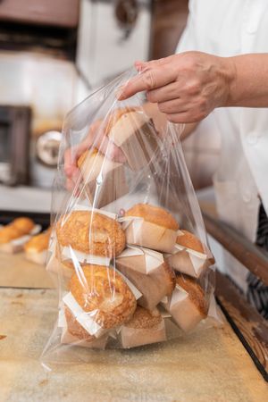 A baker woman is packing some fresh baked cupcakes into a plastic bag