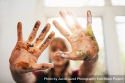 Woman with paint on her hands holding them to camera with focus on hands 56LeNb