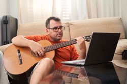 man has fun with laptop learning guitar songs online
