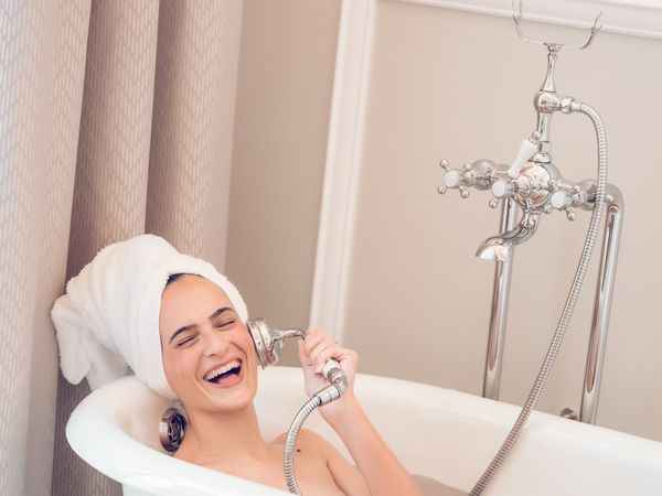 Cheerful woman in bathtub and imitating phone call with shower