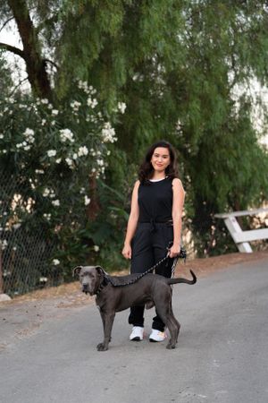 Full length shot of woman standing with her dog in front of green trees