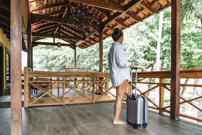 Joyful woman in bikini carrying suitcase at hotel terrace