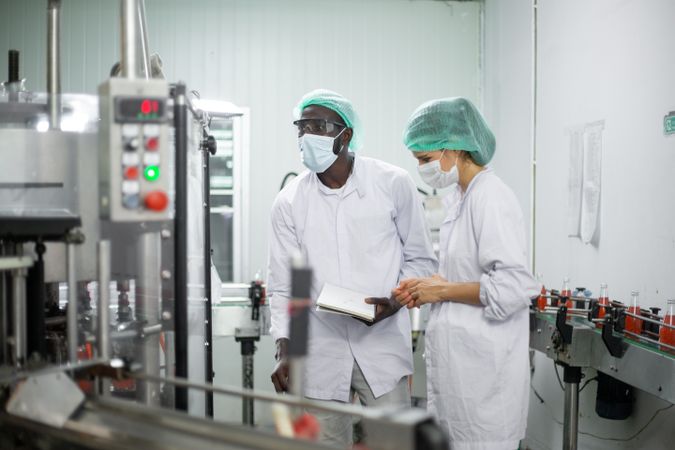Two diverse factory workers are inspecting machinery inside a beverage production facility.