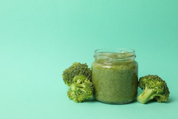 Glass jar with broccoli puree on mint background