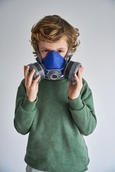 Kid in half face respirator and looking at camera in gray studio