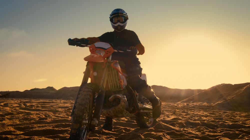 Front View Shot of the Professional Motocross Driver Saddles His FMX Dirt Bike on the Sand/ Dirt Track.